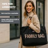 Black fabric tote bag with gold-toned 'FAMILY BAG' text, brown faux leather straps, and a small blue 'CHILDHOME' label.