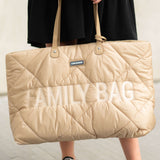 Puffy beige quilted tote bag with 'FAMILY BAG' embroidered in white. Features two beige top handles with gold-toned rivets an