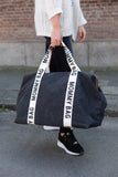 Large black canvas duffel bag with white fabric straps featuring 'MOMMY BAG' text. Brown-toned trim visible at the top openin