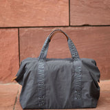 Dark grey fabric duffel bag with 'MOMMY BAG' text on its two straps and brown-toned top handles. Small brown tab on side.