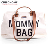 Off-white "MOMMY BAG" with black text, brown leather-look top handles, and a brown woven adjustable shoulder strap.