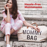 Off-white duffel bag with 'MOMMY BAG' in black letters, brown faux leather top handles and trim.