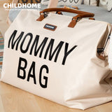 Off-white fabric duffel bag with "MOMMY BAG" in black text, brown leather-look top handles, and a "CHILDHOME" tag.