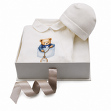 White baby sleepsuit with rounded collar and teddy bear print, paired with a matching white baby hat.