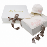 White sleepsuit with a rounded collar and matching beanie hat, both embroidered with pink 'Princess' text and a crown.