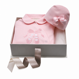 Pink infant sleepsuit with rounded collar and ballet shoe appliqué, paired with a matching pink bonnet featuring a satin bow.
