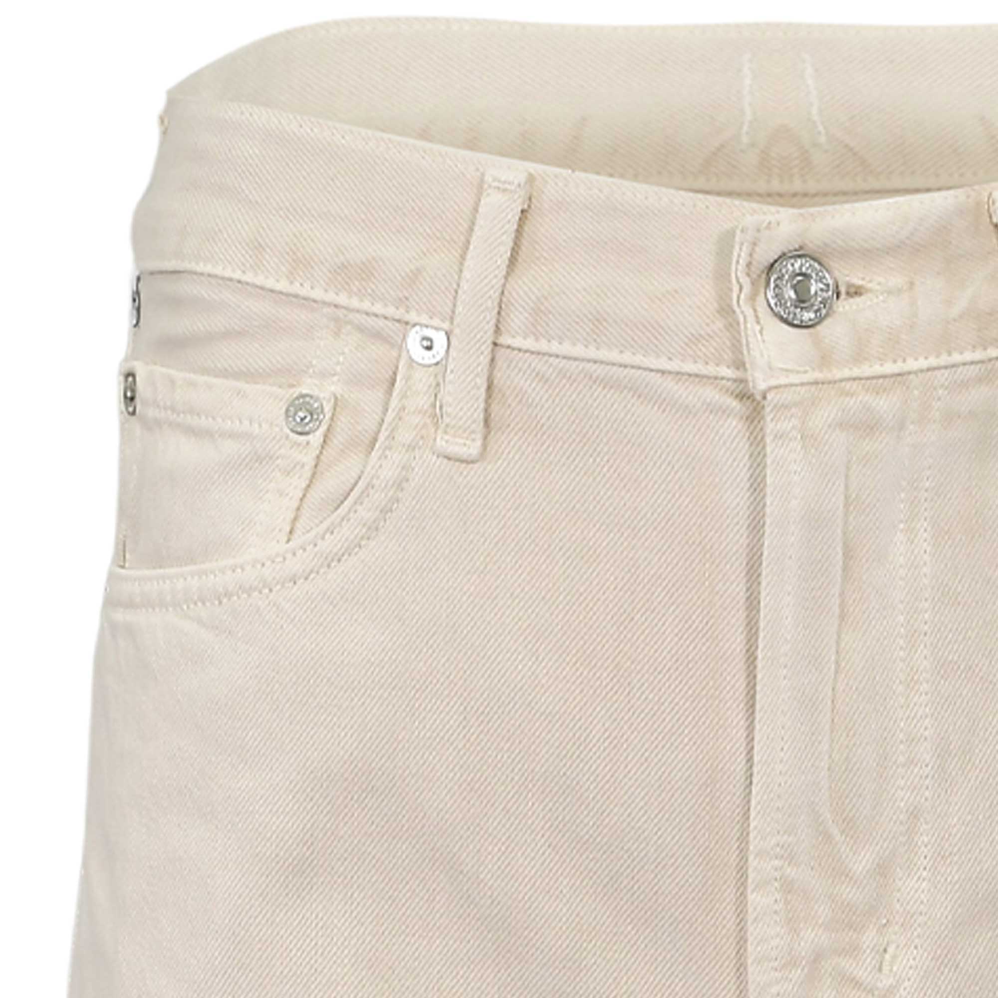 Close-up structural detail of the front waistband on the Citizens of Humanity ecru jeans, highlighting the branded metal button, fly stitching, and coin pocket.