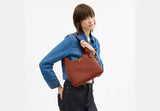 Person holding a brown leather bag against a white background.