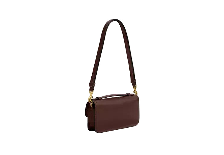 Side-profile view of the Coach Hamptons bag in dark maple leather, showcasing its slim depth and adjustable shoulder strap.