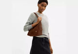 Woman holding a brown leather bag against a white background.