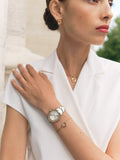 Still life collection layout highlighting the Marina gold earrings alongside the matching monogram necklace, bracelet, and a green leather luxury watch.