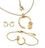 A studio display of the all-gold Aigner Matila jewelry set, showing the short cable chain necklace with its crystal-embellished crescent pendant, matching open-hoop earrings, and the adjustable chain bracelet featuring the gold-tone hexagonal logo hardware.