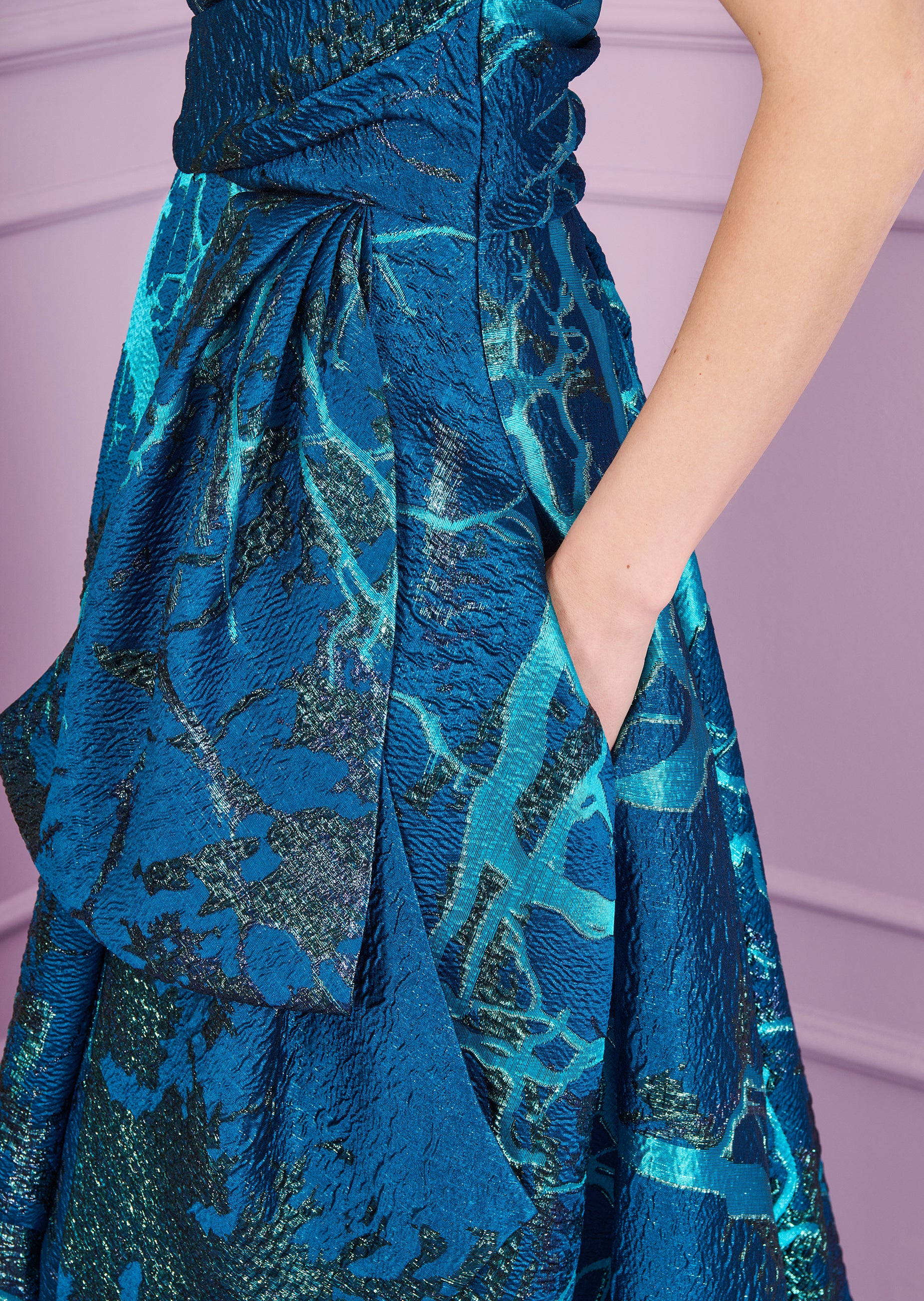 Teal long dress with a textured, abstract blue-green pattern. Features a ruched bodice, a large draped bow on the left, and a