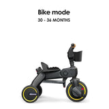 Black Doona Liki Trike S5 with three wheels, yellow accents on rims, black seat, small basket, and tan handlebar grip.