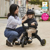 Black Doona Liki Trike S5 with three wheels, black frame, black seat, black handlebars with wood-toned grips, and gold-toned