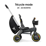 Black and dark gray trike with yellow wheel rims, a silver-toned push handle, black storage bag, and a wood-toned handlebar g