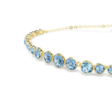 A detailed macro close-up shot focusing on the focal strand of the Swarovski Imber bracelet, emphasizing the flawless alignment of the smooth gold bezel-set, round-cut blue clear crystals.