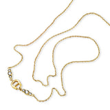 A close-up studio overview of the Aigner Iva yellow gold necklace beautifully coiled on a white surface, highlighting the polished 'A' logo emblem flanked by graduated bezel-set clear crystals and the fluid construction of the chain links.