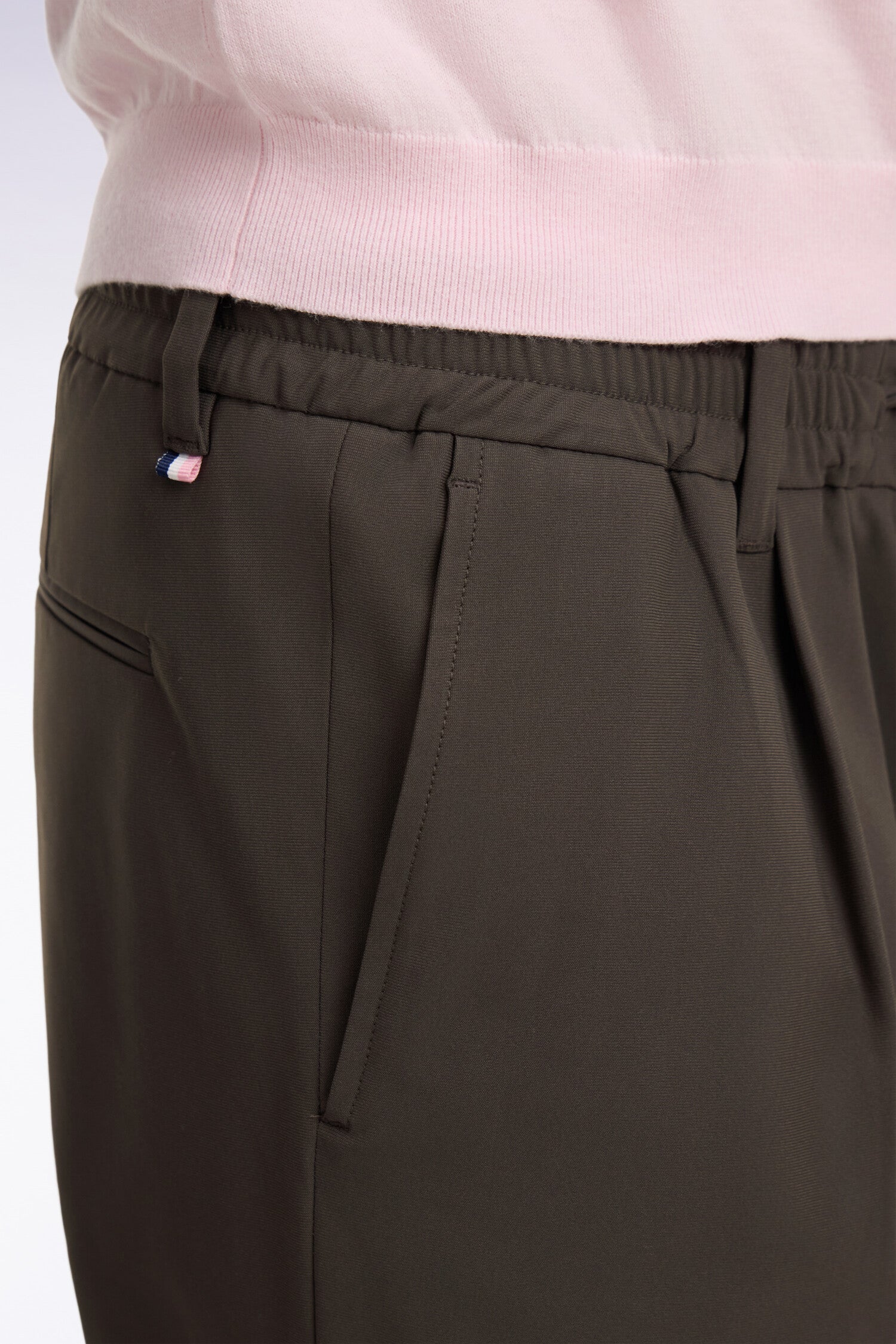 Dark olive green trousers with an elasticated waistband, belt loops, side slash pockets, and a back welt pocket. Small tricol