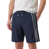 Navy blue swim shorts with white drawstring, tips. Each side has two white vertical stripes, 'EMPORIO ARMANI' text on the rig