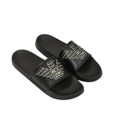 Black beachwear slide slippers. Each has a wide strap with a white outline of an eagle logo. "EMPORIO ARMANI" is embossed on
