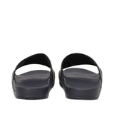 Pair of black beachwear slides with wide foot straps and solid black soles, viewed from the rear.