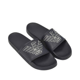 A pair of black slide slippers. Each slipper has a wide strap with a white outlined eagle logo.