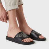 Black slide slippers with a wide strap. A white outline of the Emporio Armani eagle logo is on the strap. 'EMPORIO ARMANI' is
