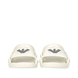 Pair of off-white rubber slide slippers. Each slipper has a wide strap with a black eagle logo inside a circle.