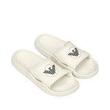 Pair of white slide sandals with a wide top strap featuring a black circular logo with horizontal stripes. Textured footbed.