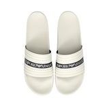 Pair of white slide slippers with ribbed straps. Each strap has a black band with 'EMPORIO ARMANI' and eagle logo in white.