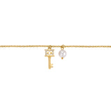 Gold-toned chain bracelet with a key charm featuring a crystal-encrusted 'CC' bow and a white pearl charm.