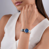 Silver-toned watch with a round case, blue mother-of-pearl dial, four diamond markers, and a silver-toned link bracelet.