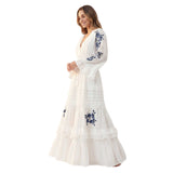 Woman wearing a white dress with blue floral embroidery on a white background.