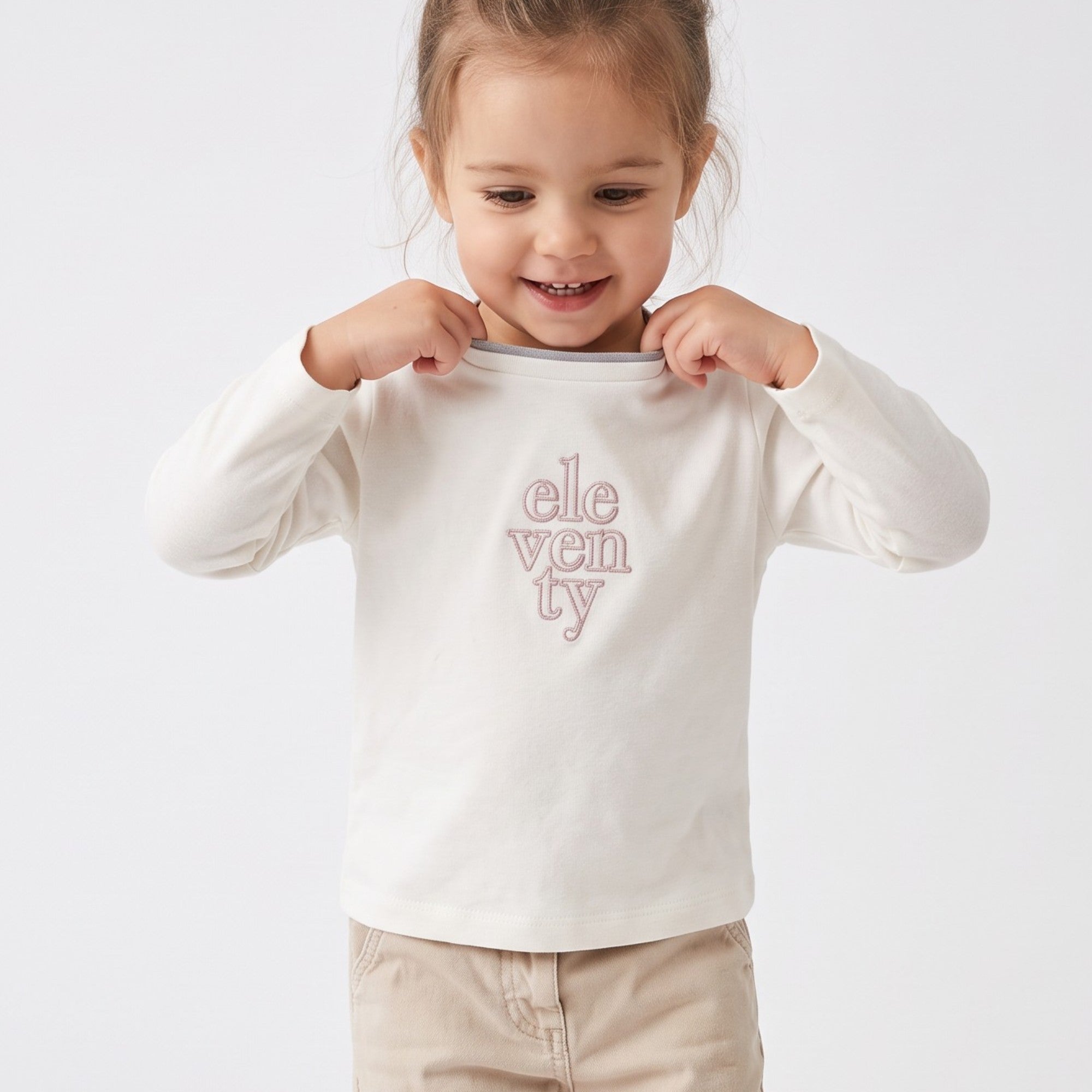 Ivory long-sleeve t-shirt with a grey-trimmed crew neck and "eleventy" embroidered in light pink outline on the front.
