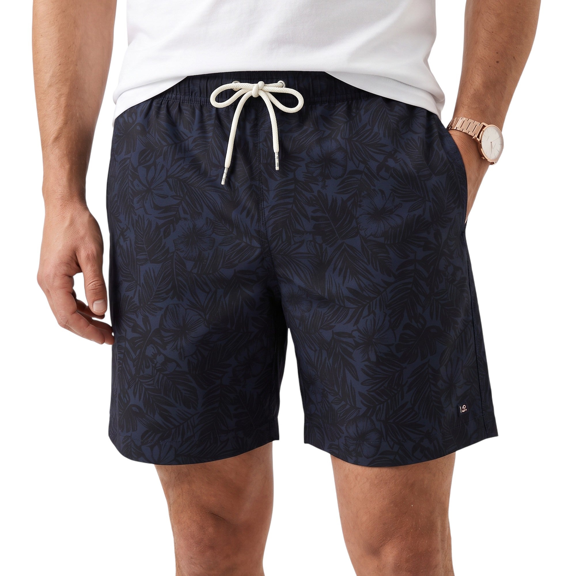 Front close-up studio shot of a male model wearing the navy tropical Eden Park swim shorts, styled with a casual white t-shirt and a gold-tone watch.