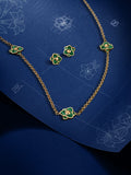 An editorial lifestyle image displaying the Burj jewelry collection on a textured deep blue blueprint backdrop, featuring the malachite flower necklace alongside matching stud earrings and design sketches.