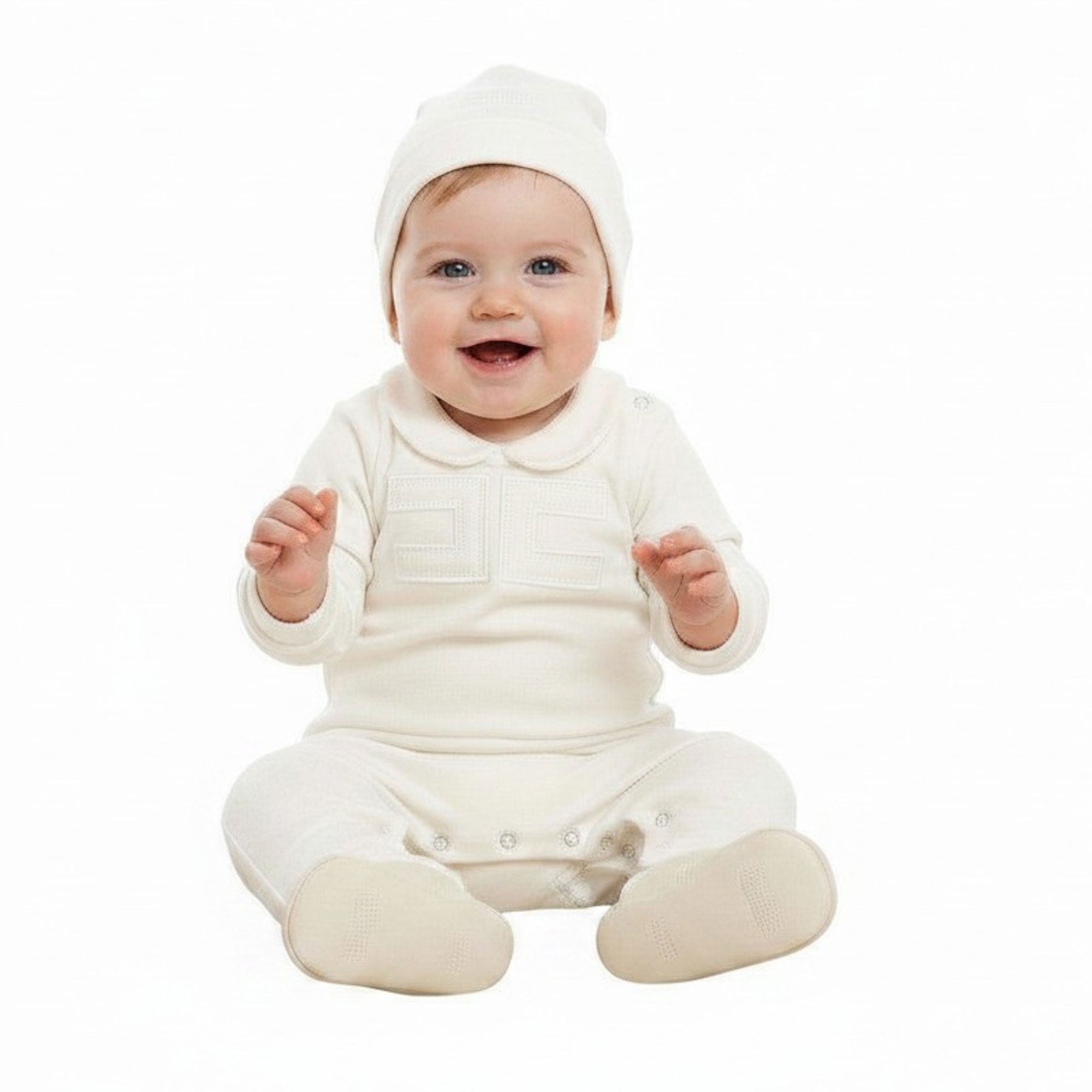 A smiling baby sitting down against a white background, wearing an off-white Elisabetta Franchi footed romper with a chest logo patch and a matching knit beanie.