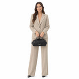 Woman in a beige suit holding a black handbag on a white background.