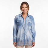 Front view of a smiling model wearing the Ermanno Firenze light blue chambray shirt unbuttoned over a camisole and paired with light neutral trousers.