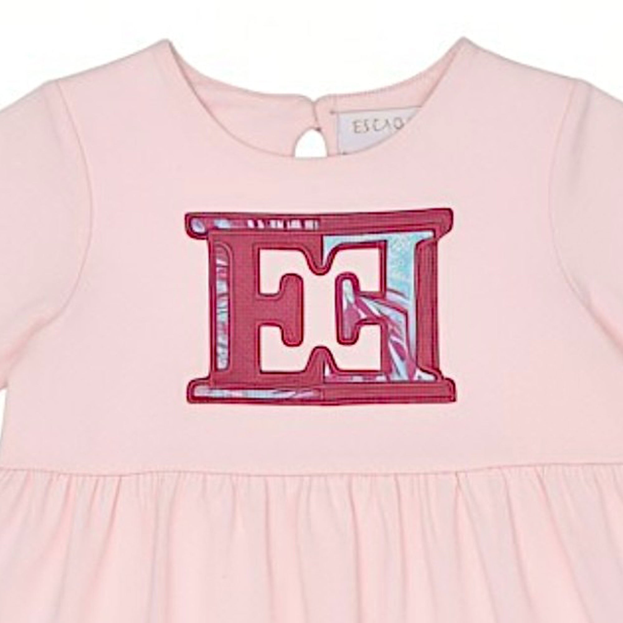 Close-up shot focusing on the upper front bodice of the Escada Kids dress, detailing the round neckline and the embroidered pink "EE" logo emblem with its abstract patterned fill.