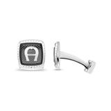 A high-resolution studio presentation of the Aigner Emilio men's cufflinks showing one cufflink face-forward to reveal the rounded square silver frame, dark grey brick-textured inlay, and central silver horseshoe logo, beside another cufflink profile showcasing its curved post and swivel toggle mechanism.