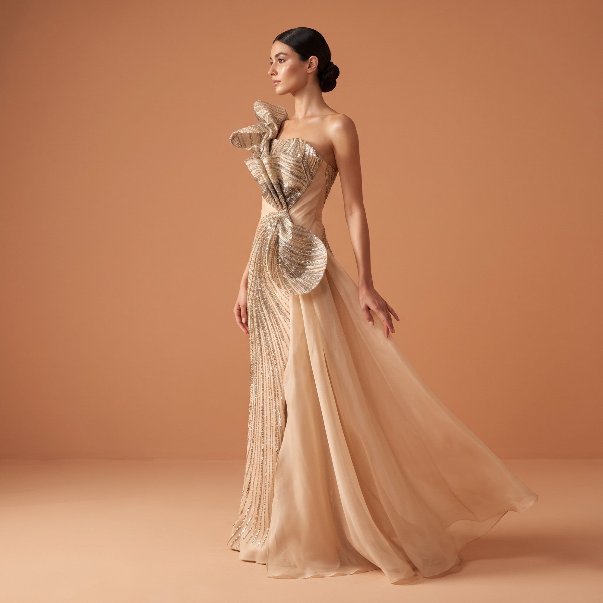 Gold one-shoulder floor-length gown with intricate sequin embellishments, ruffled shoulder, and a flowing sheer skirt overlay