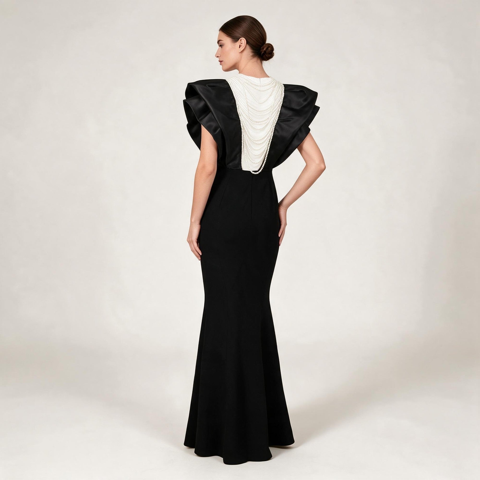 Black mermaid dress with large ruffled black satin shoulders and a white back panel draped with multiple strands of white pea