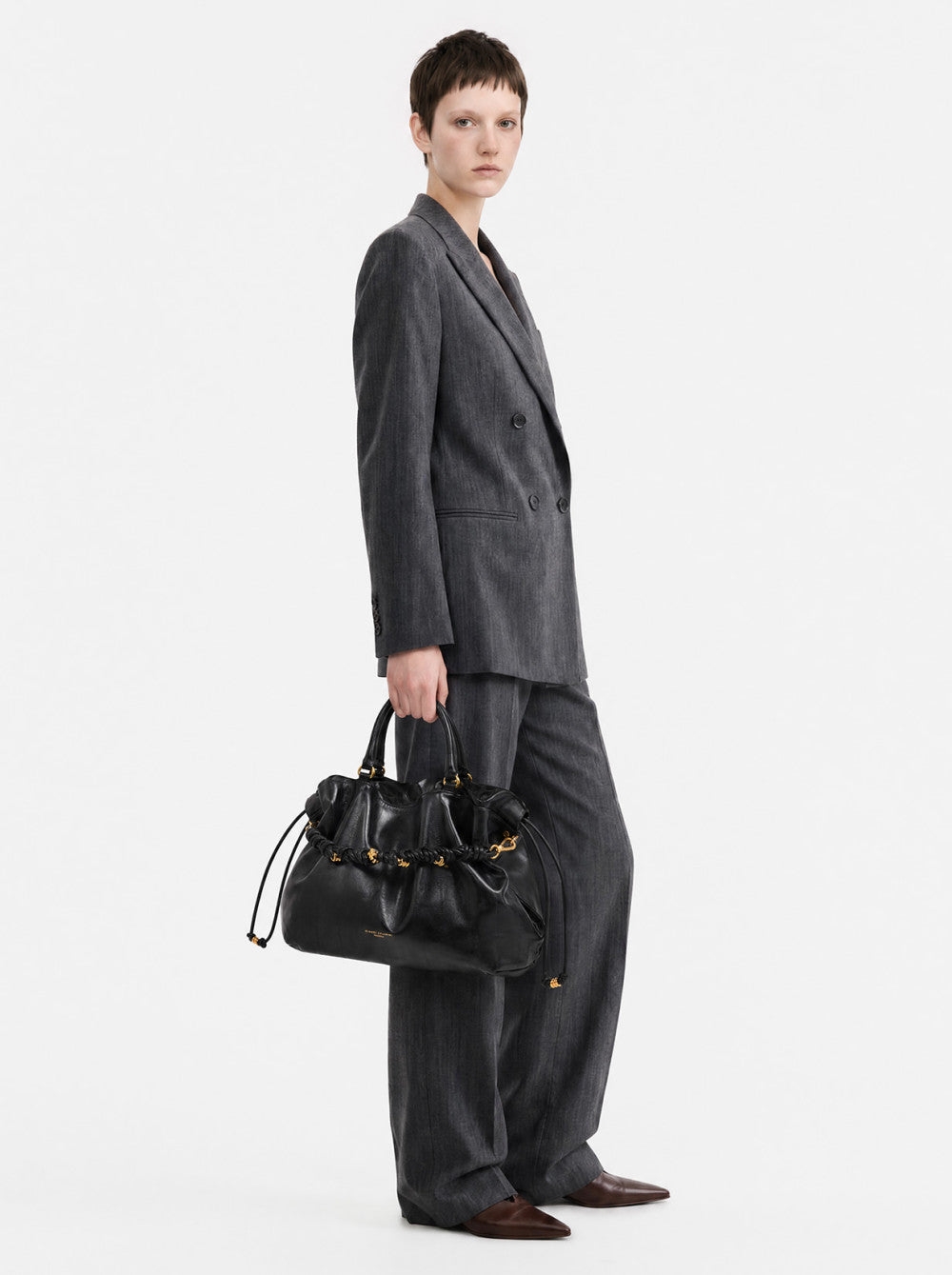 Black leather handbag with a gathered drawstring top, two short handles, and gold-toned hardware featuring a decorative braid
