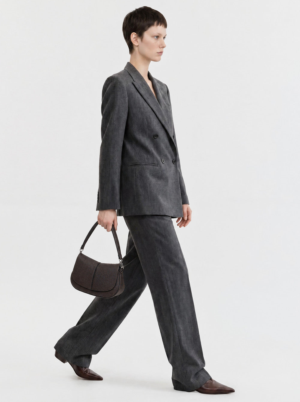 Textured dark brown round handbag with a curved flap, central front seam, single strap, and silver-toned hardware.