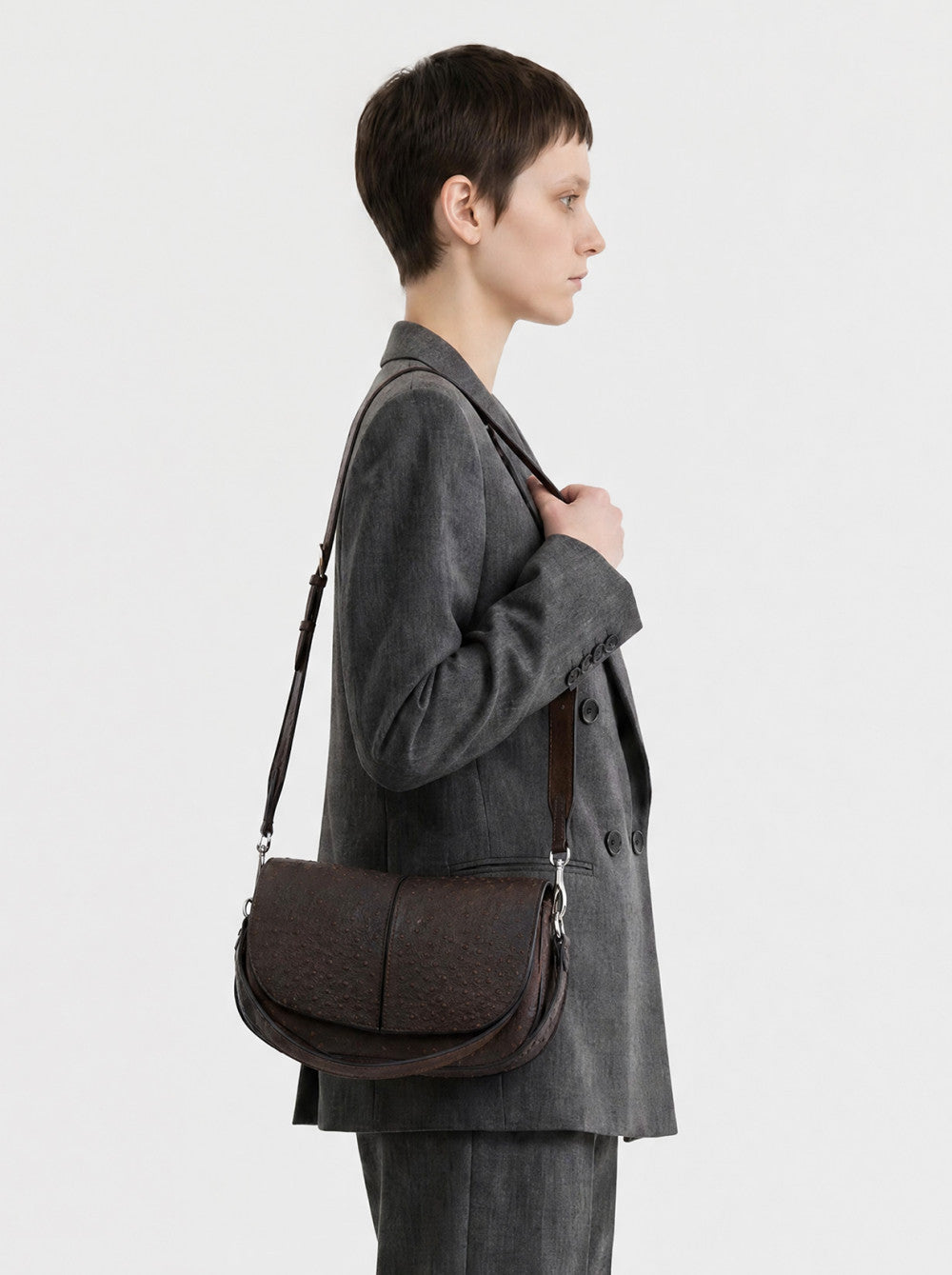 Dark brown textured leather round handbag with a curved flap, adjustable shoulder strap, and silver-toned hardware.
