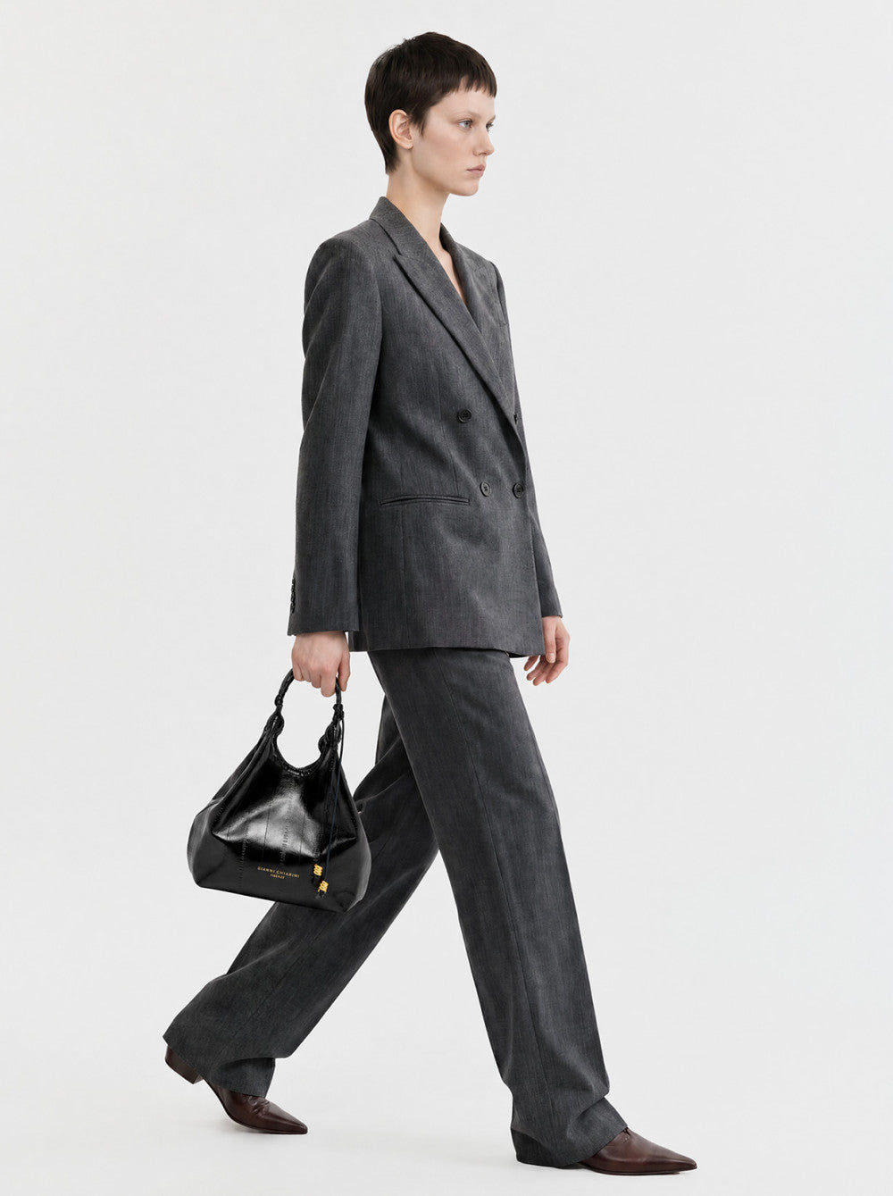 Black textured leather hobo bag with a braided top handle, drawstring closure, and gold-toned logo plaque and hardware.