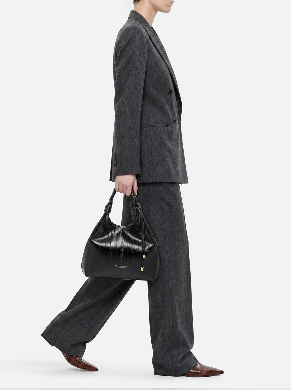 Black leather hobo bag with a braided top handle, textured central panel, gold-toned drawstrings, and feet.