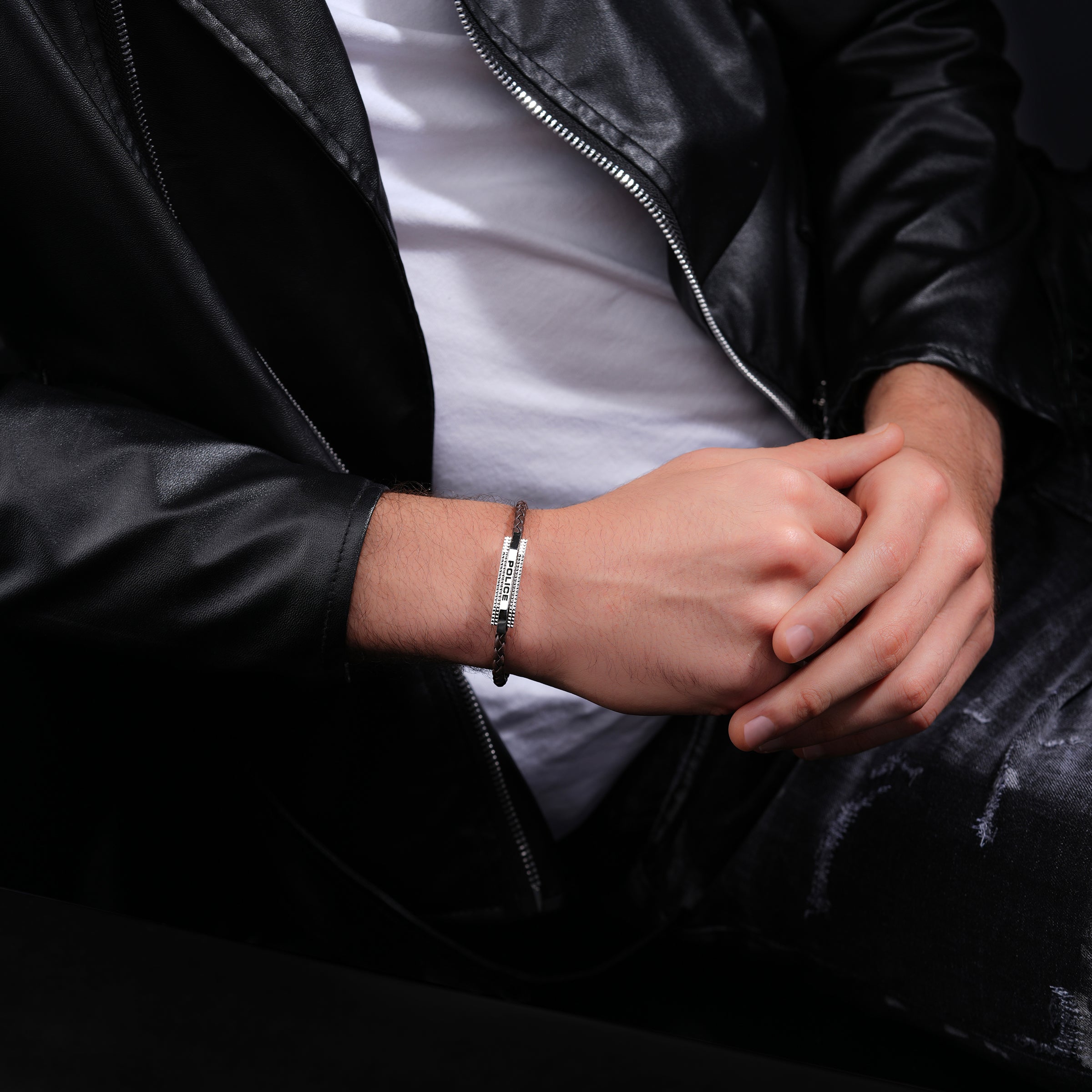 Brown braided leather bracelet with a silver-toned rectangular bar featuring vertical "POLICE" engraving and studded edges.
